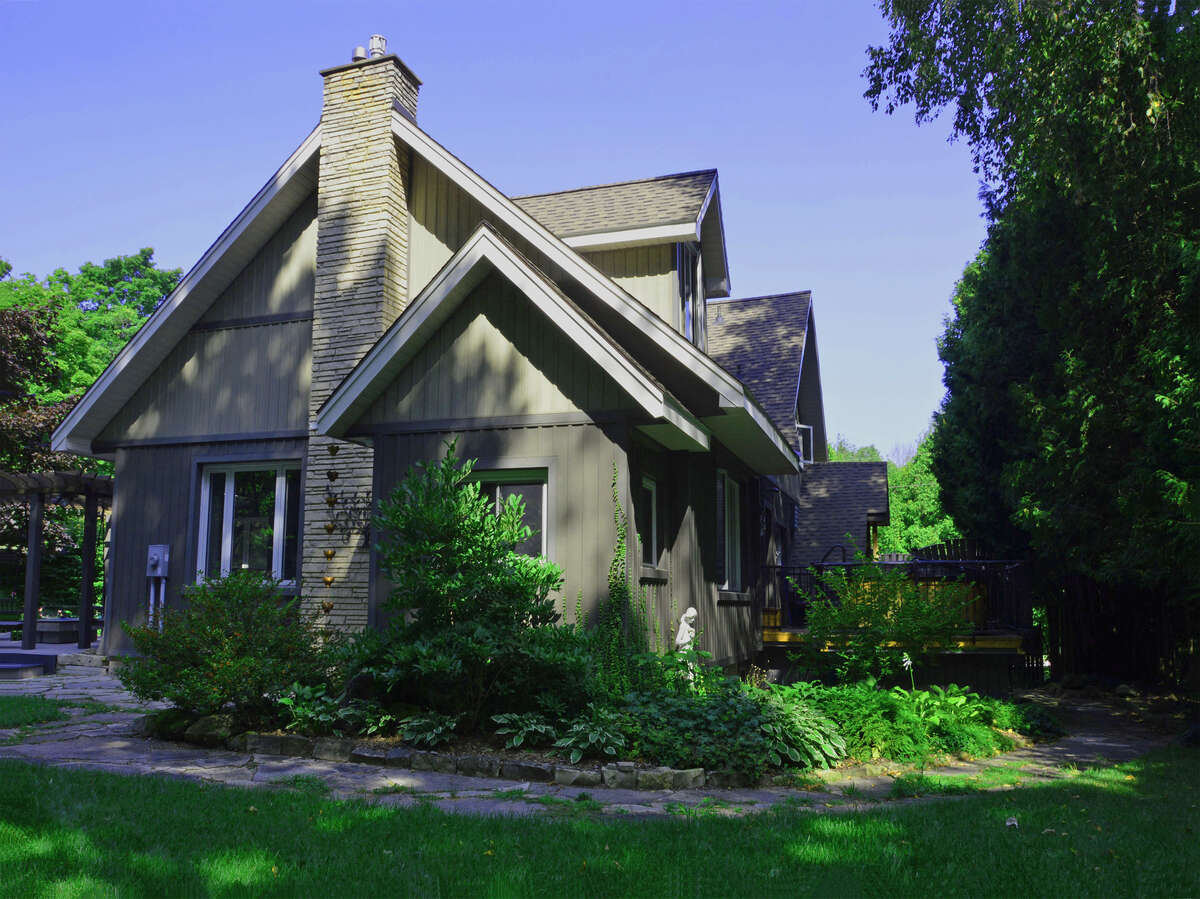 Charming side view with stone chimney, lush gardens, and path leading to the backyard oasis.