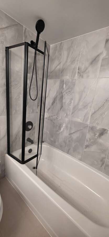 New primary bathroom wall and floor tiles with minimalist foldable glass tub enclosure