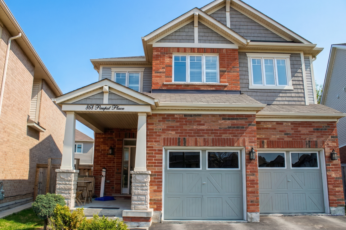 View of front of house with a double garage, red rustic style brick siding, and front door way.