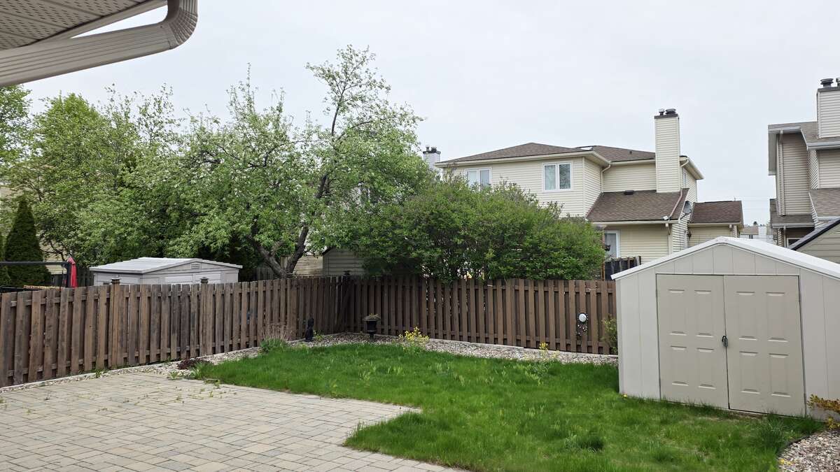 Fully fenced backyard with paver patio, lawn, and storage shed
